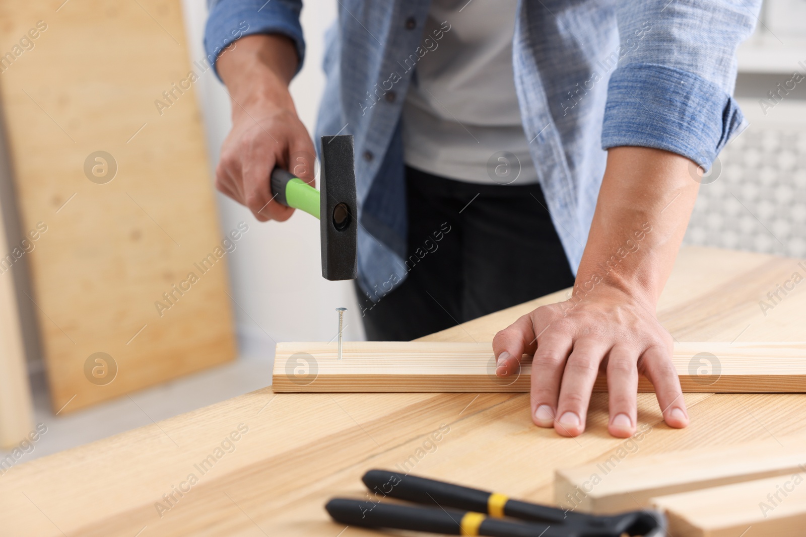 Man hammering nail into wooden plank indoors, closeup. Space for text Photo of Man hammering nail into wooden plank indoors, closeup. Space for text