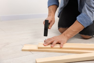 Photo of Man hammering nail into wooden plank indoors, closeup. Space for text