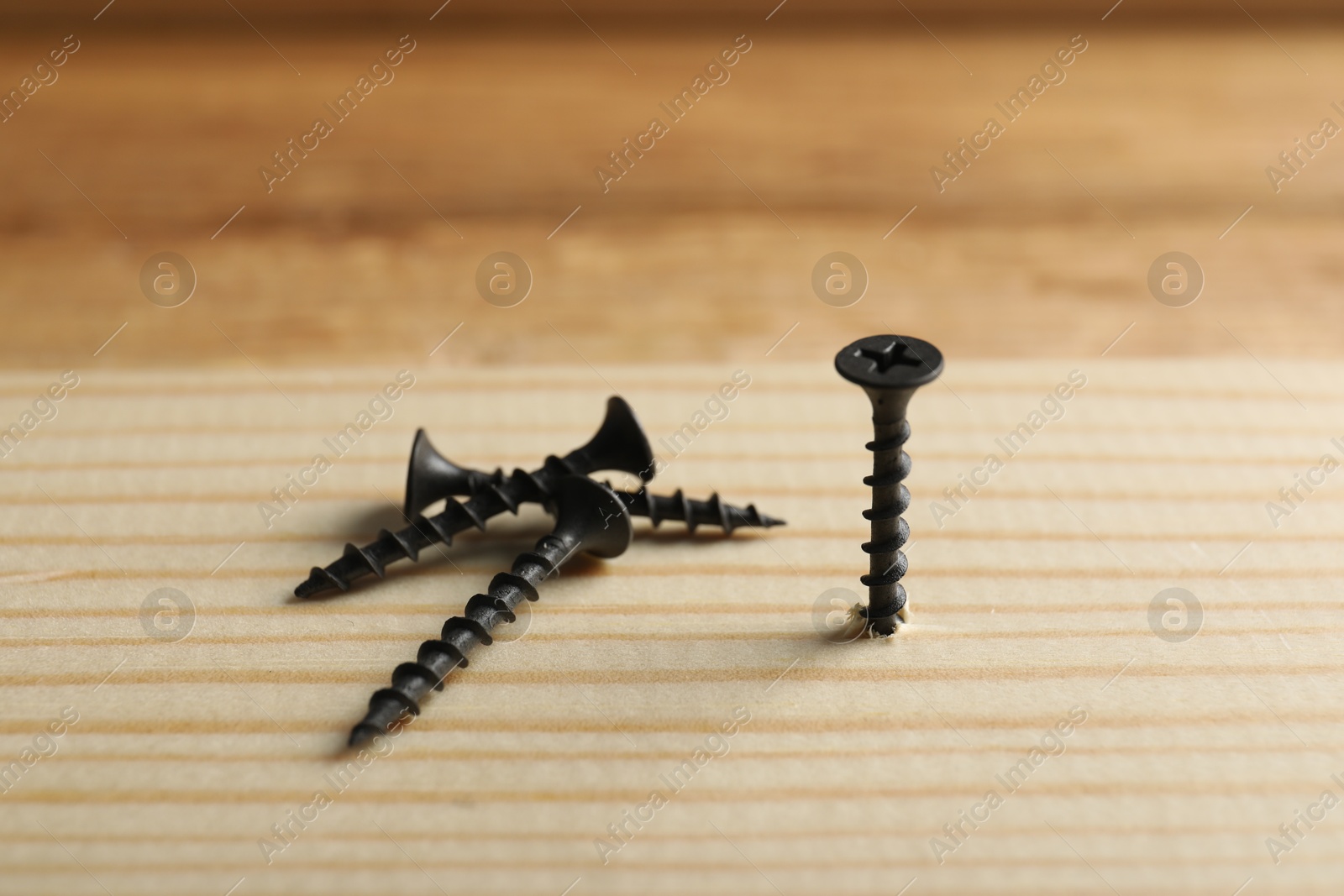 Photo of Metal screws and wooden plank on table, closeup