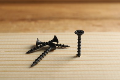 Photo of Metal screws and wooden plank on table, closeup