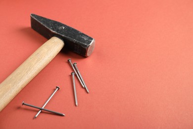 Photo of Metal nails and hammer on coral background, closeup. Space for text