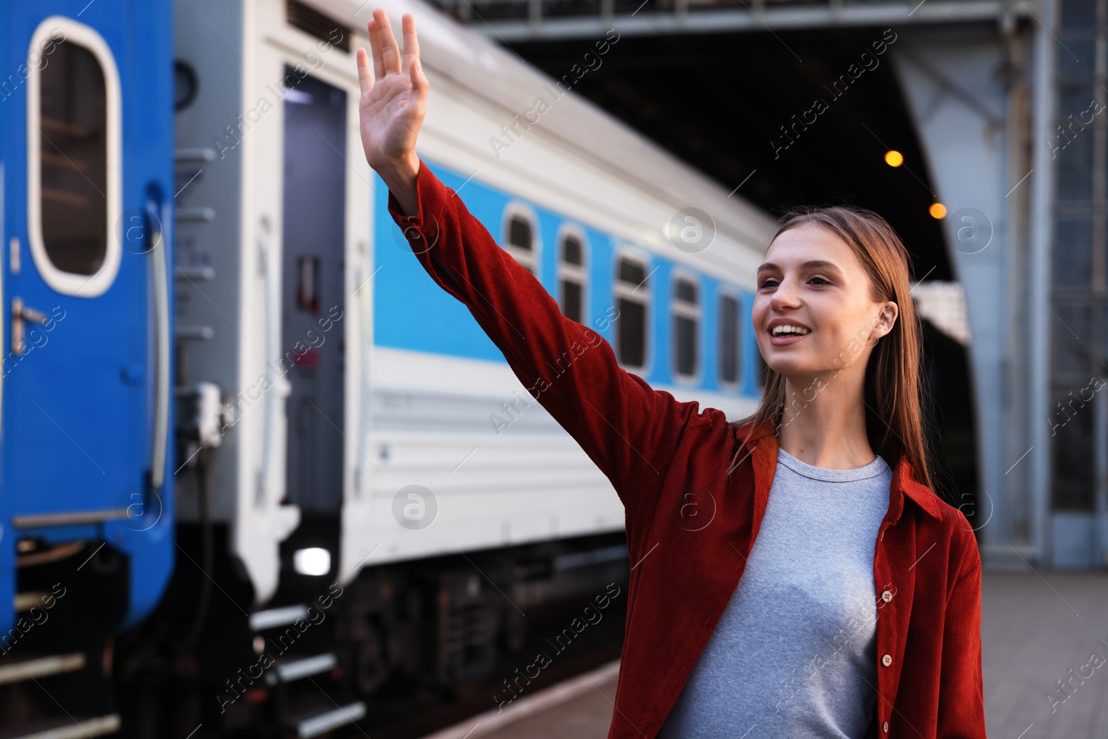 Photo of Goodbye. Happy woman waving near train outdoors