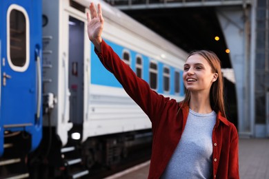 Photo of Goodbye. Happy woman waving near train outdoors