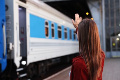 Photo of Goodbye. Woman waving near train outdoors, back view. Space for text