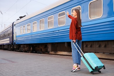 Photo of Goodbye. Happy woman with luggage waving near train outdoors