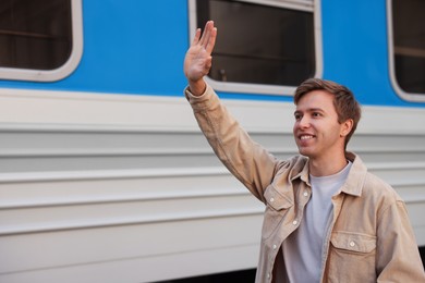 Photo of Goodbye. Happy man waving near train outdoors, space for text