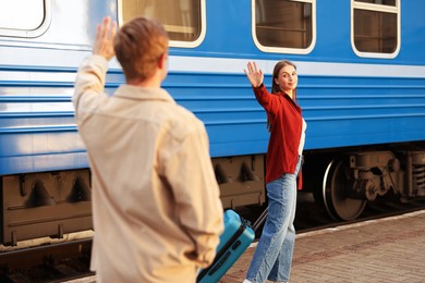Photo of Goodbye. Man waving to his girlfriend near train outdoors, selective focus