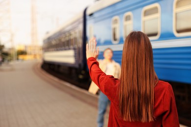 Photo of Goodbye. Woman waving to her boyfriend near train outdoors, selective focus