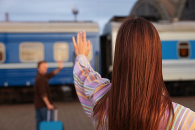 Photo of Goodbye. Woman waving to her boyfriend on platform of railway station, selective focus