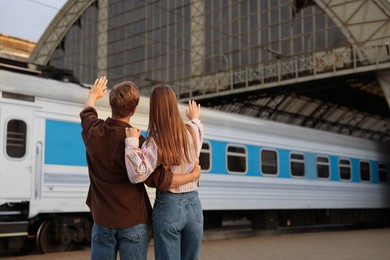 Photo of Goodbye. Couple waving on platform of railway station, back view. Space for text