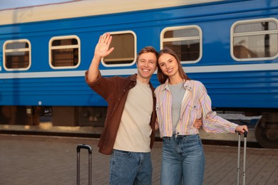 Photo of Goodbye. Couple with suitcases waving on platform of railway station
