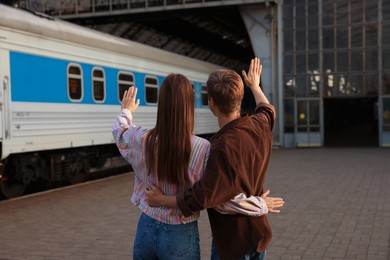 Photo of Goodbye. Couple waving on platform of railway station, back view