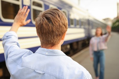 Photo of Goodbye. Man waving to his girlfriend near train outdoors, selective focus