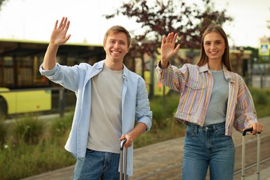 Photo of Goodbye. Lovely couple with suitcases waving at bus stop