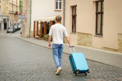 Photo of Goodbye. Man with luggage walking outdoors, back view