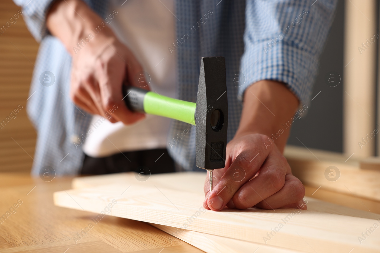 Photo of Man hammering nail into wooden plank indoors, closeup