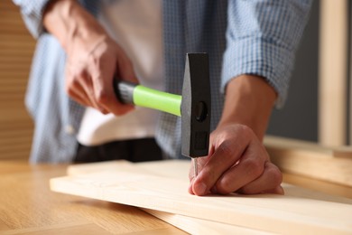 Photo of Man hammering nail into wooden plank indoors, closeup
