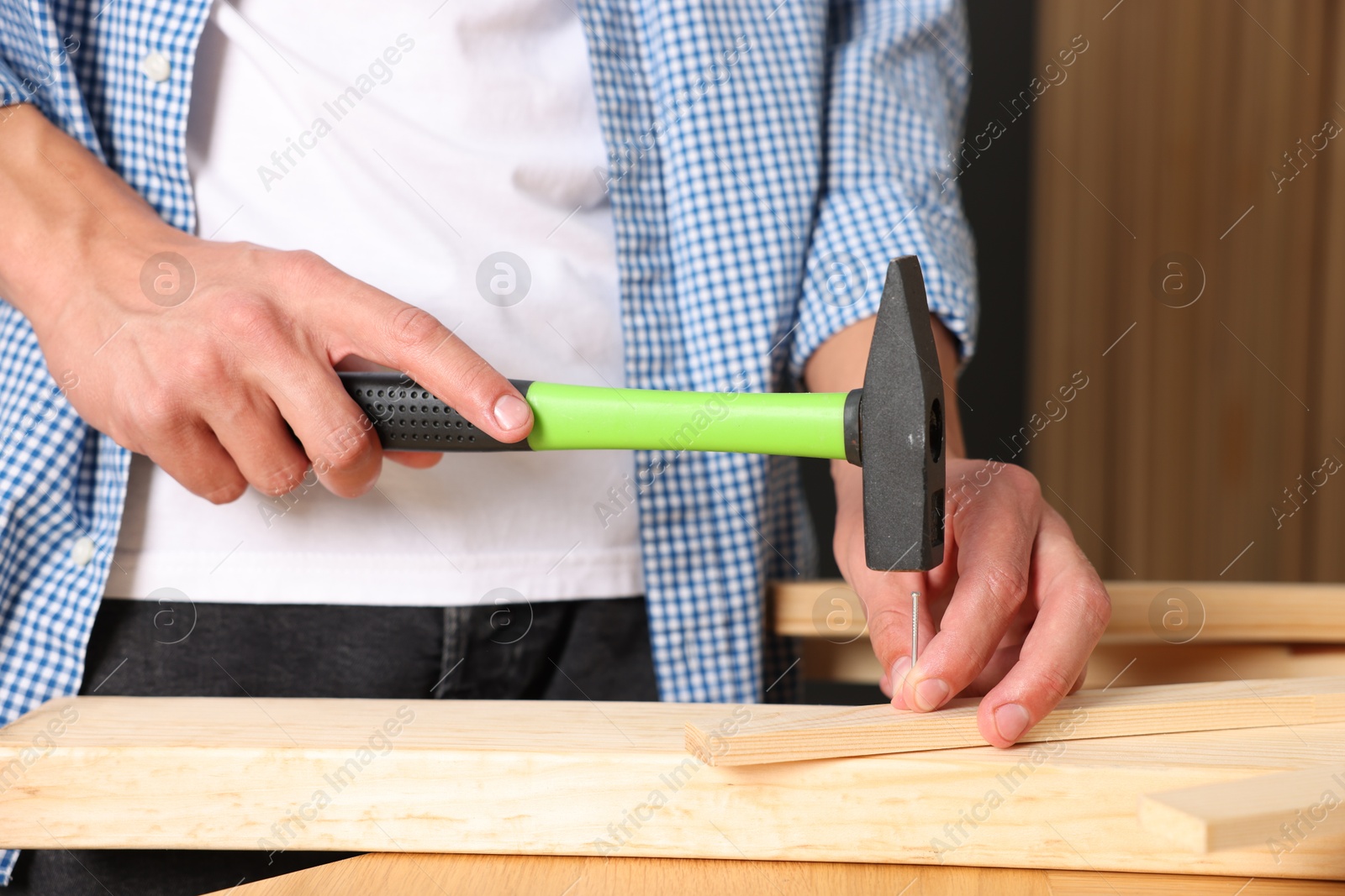 Photo of Man hammering nail into wooden plank indoors, closeup