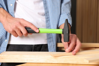 Photo of Man hammering nail into wooden plank indoors, closeup