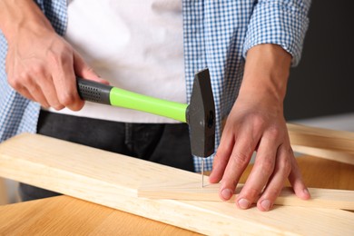 Photo of Man hammering nail into wooden plank indoors, closeup