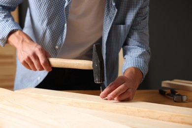 Photo of Man hammering nail into wooden plank indoors, closeup
