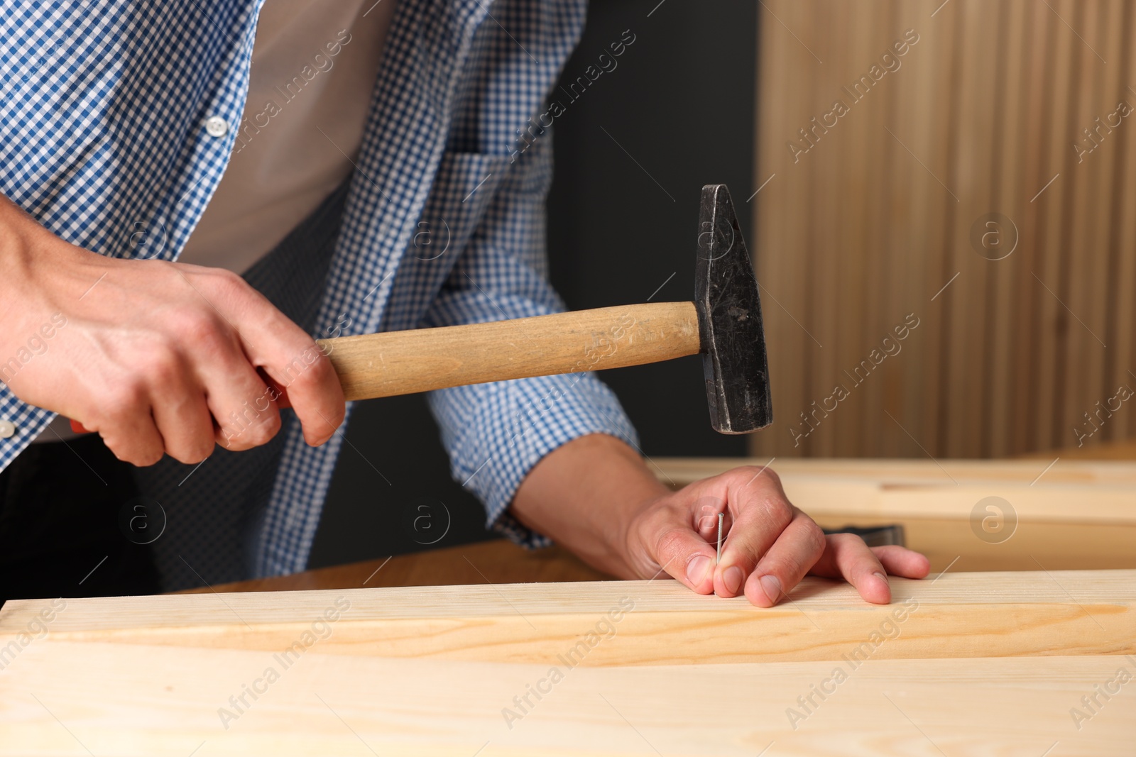 Photo of Man hammering nail into wooden plank indoors, closeup