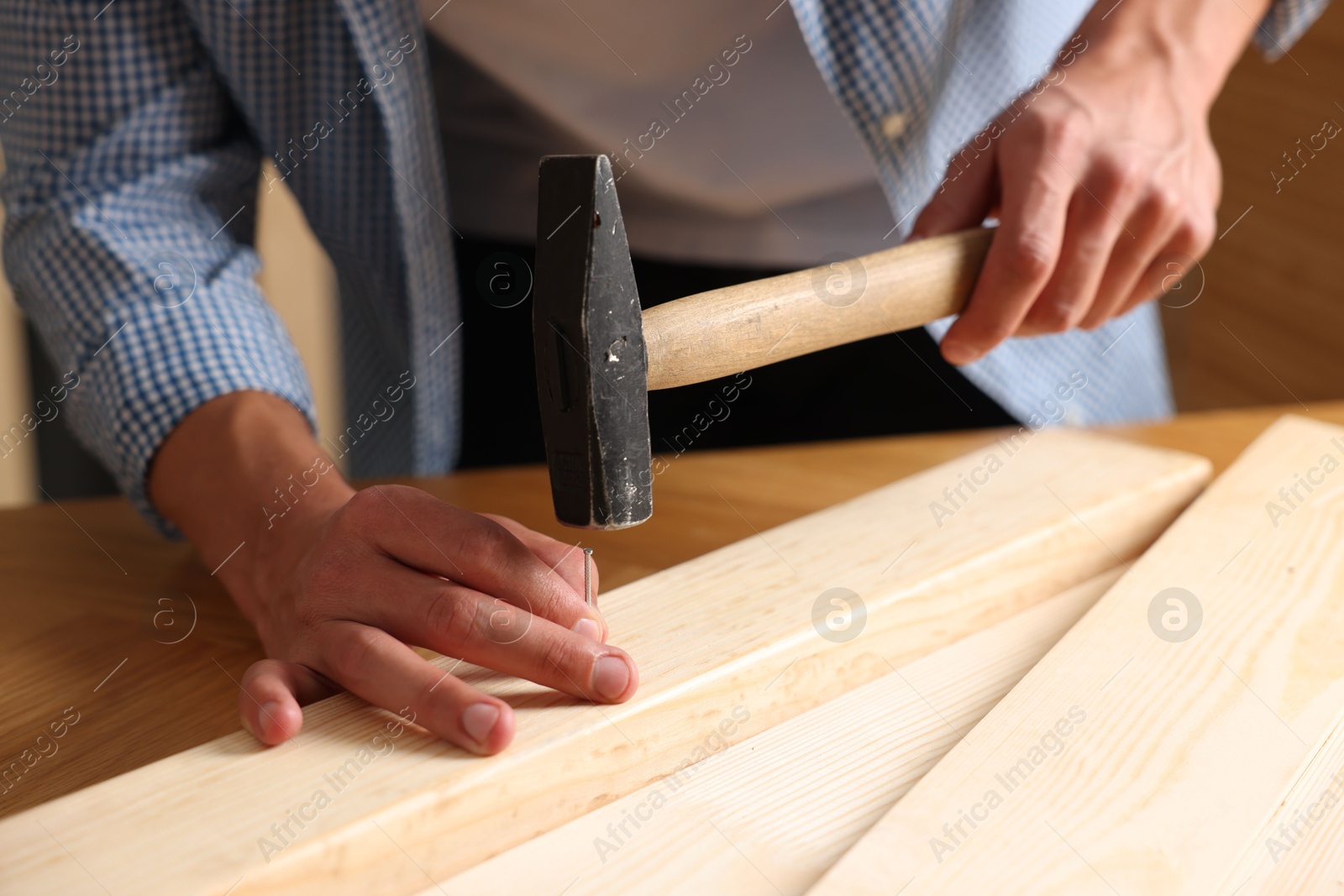 Photo of Man hammering nail into wooden plank indoors, closeup