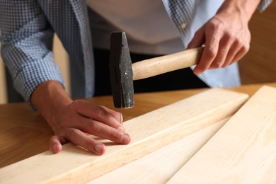 Photo of Man hammering nail into wooden plank indoors, closeup