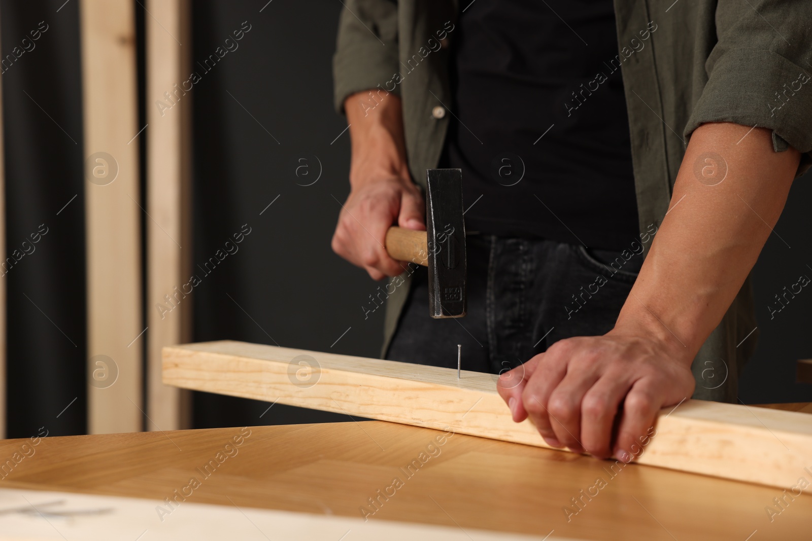 Photo of Man hammering nail into wooden plank indoors, closeup