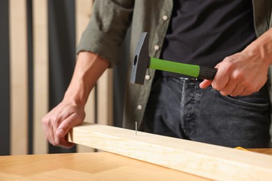 Photo of Man hammering nail into wooden plank indoors, closeup