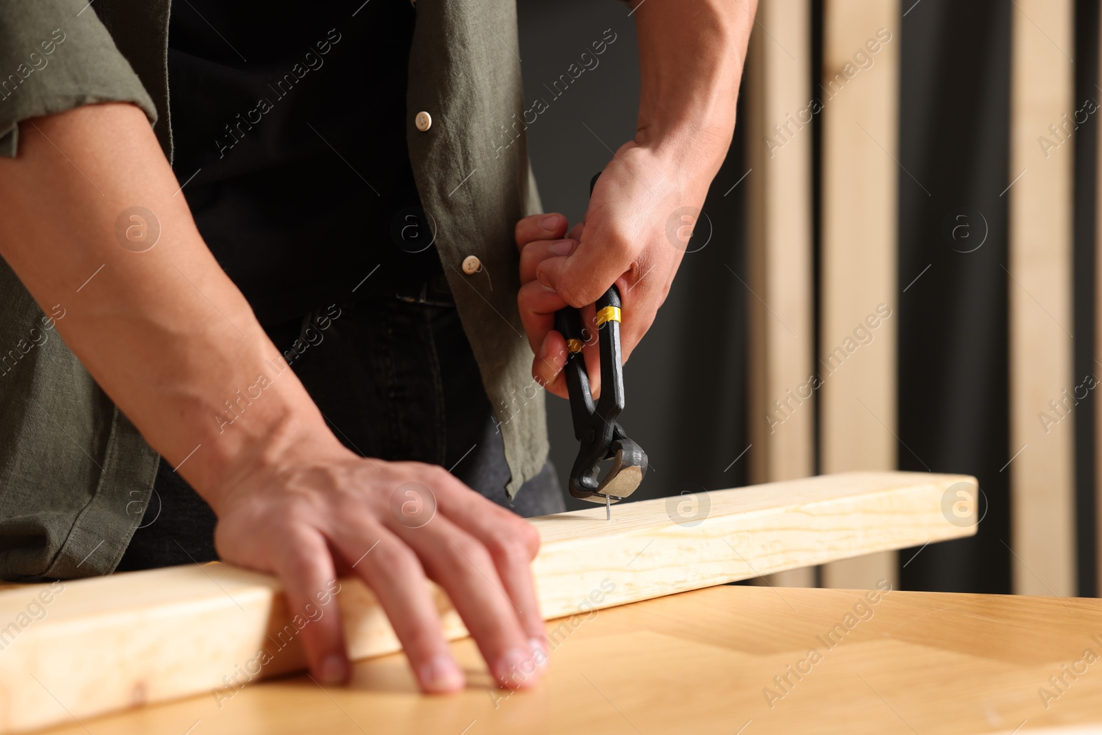 Man pulling nail out of wooden plank with pincers indoors, closeup Photo of Man pulling nail out of wooden plank with pincers indoors, closeup