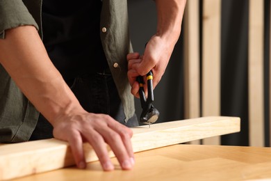 Photo of Man pulling nail out of wooden plank with pincers indoors, closeup