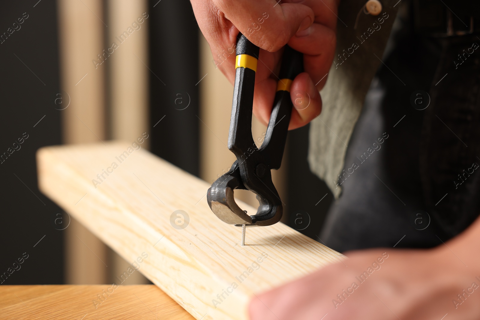 Man pulling nail out of wooden plank with pincers indoors, closeup Photo of Man pulling nail out of wooden plank with pincers indoors, closeup