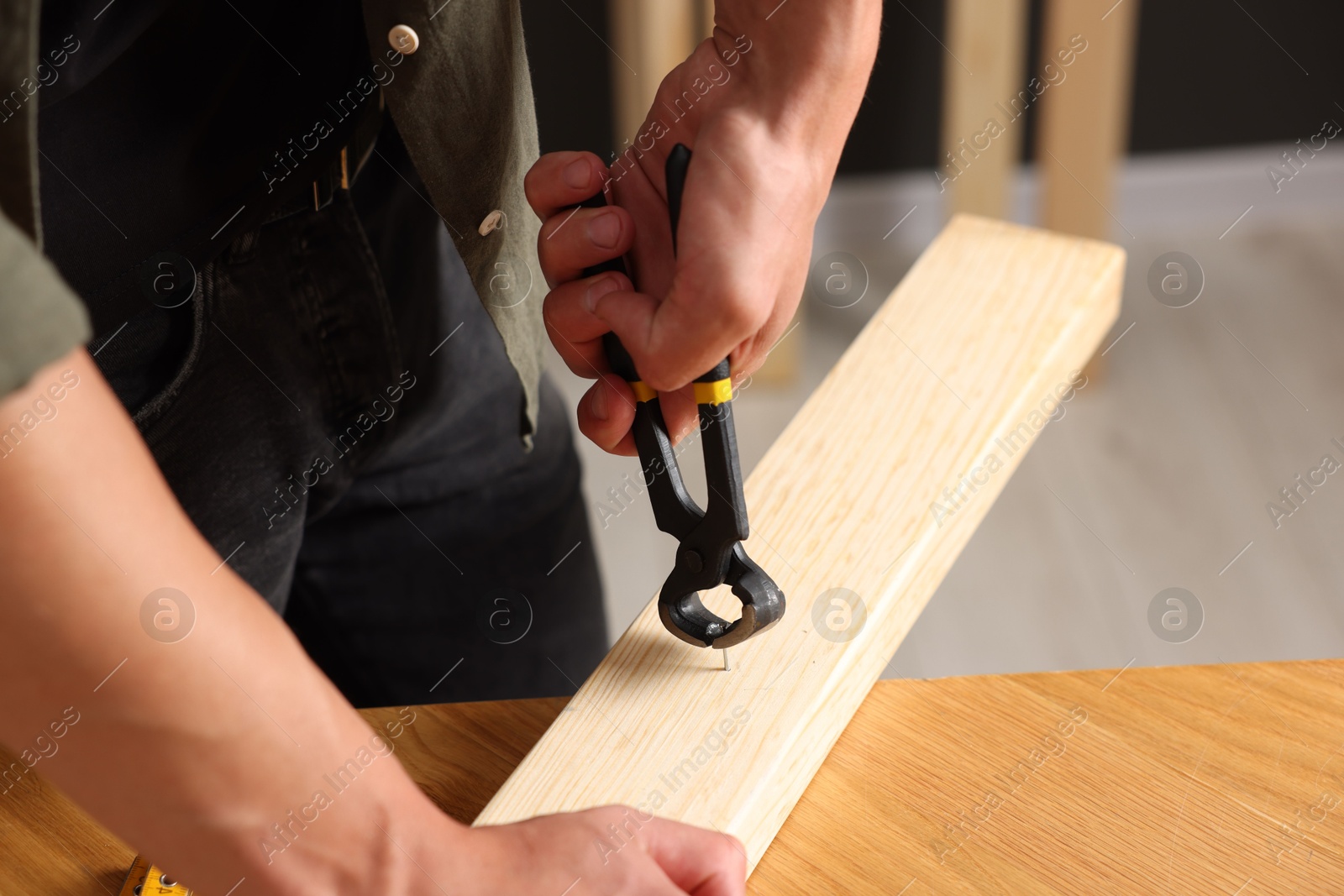 Photo of Man pulling nail out of wooden plank with pincers indoors, closeup
