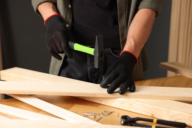 Photo of Man hammering nail into wooden plank indoors, closeup