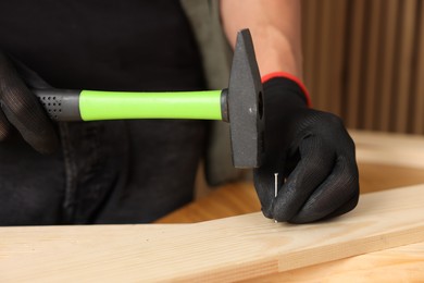 Photo of Man hammering nail into wooden plank indoors, closeup