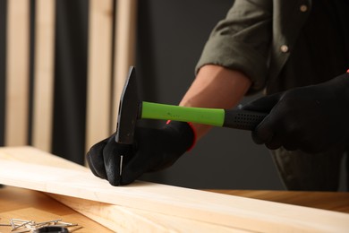 Photo of Man hammering nail into wooden plank indoors, closeup