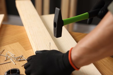 Photo of Man hammering nail into wooden plank indoors, closeup