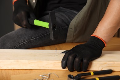 Photo of Man hammering nail into wooden plank indoors, closeup