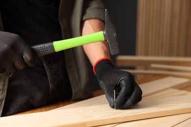 Photo of Man hammering nail into wooden plank indoors, closeup