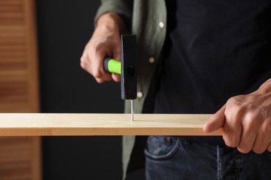 Photo of Man hammering nail into wooden plank indoors, closeup