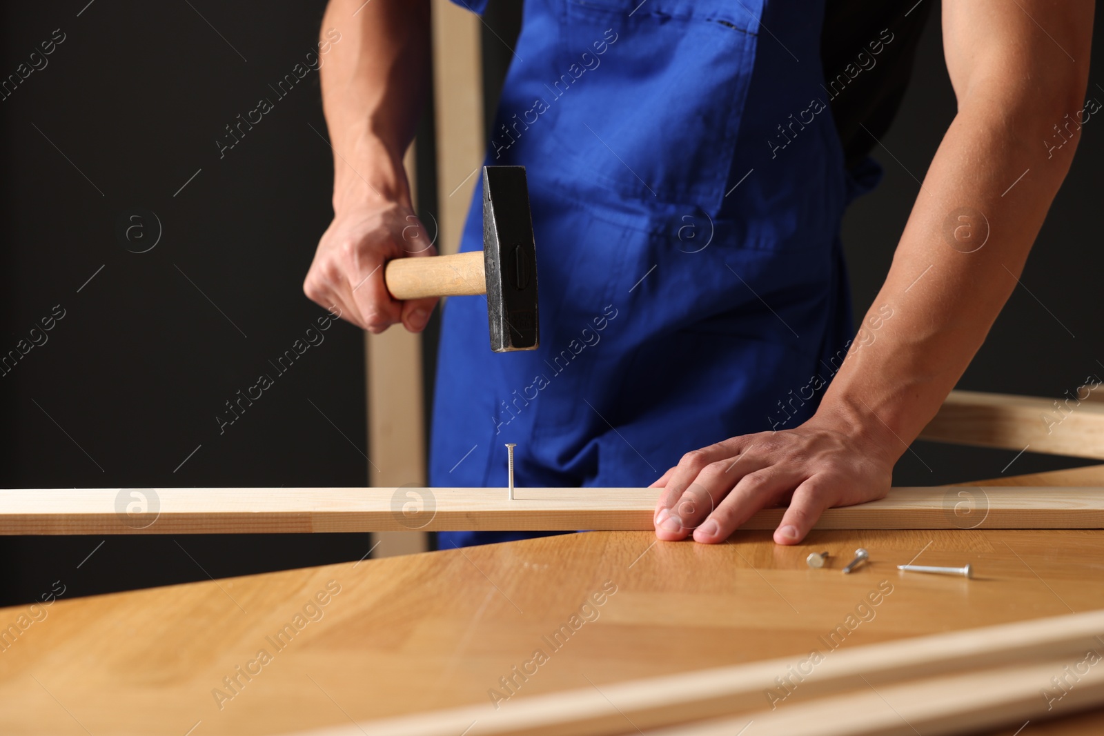 Photo of Professional repairman hammering nail into wooden plank indoors, closeup