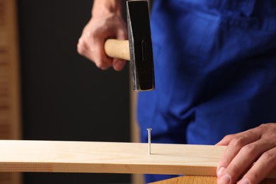 Photo of Professional repairman hammering nail into wooden plank indoors, closeup. Space for text