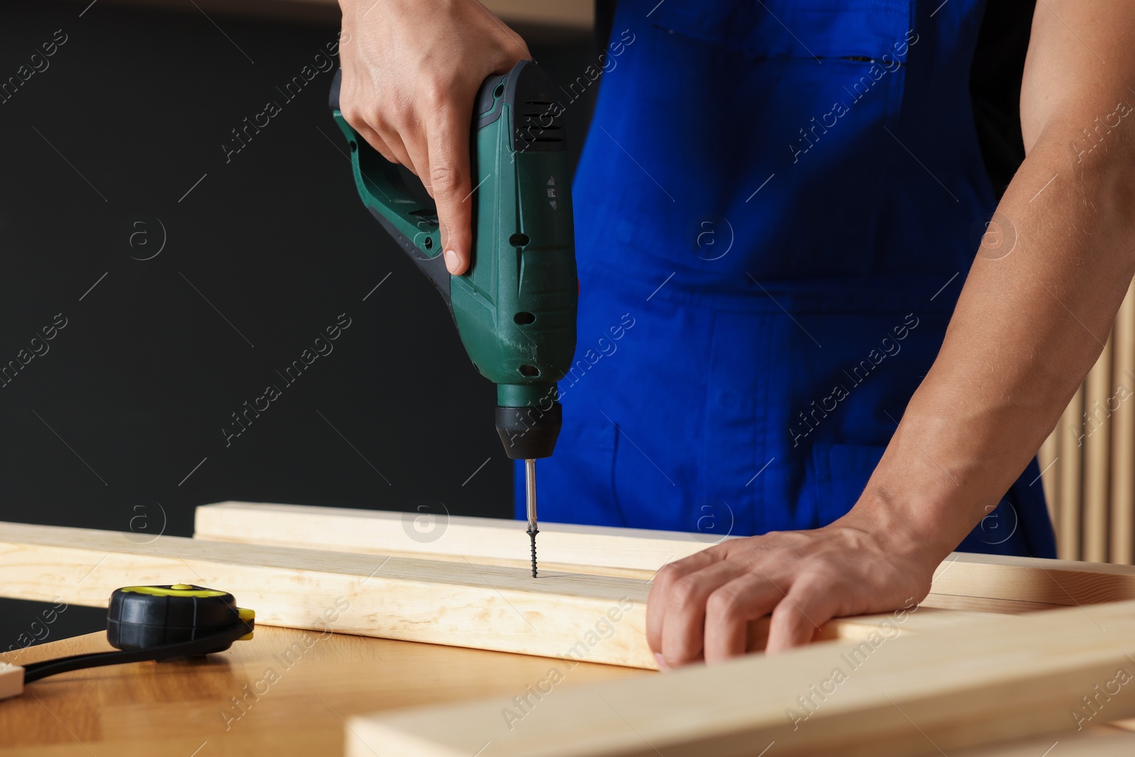 Professional repairman twisting screw into wooden plank with electric screwdriver indoors, closeup Photo of Professional repairman twisting screw into wooden plank with electric screwdriver indoors, closeup