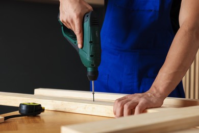 Photo of Professional repairman twisting screw into wooden plank with electric screwdriver indoors, closeup