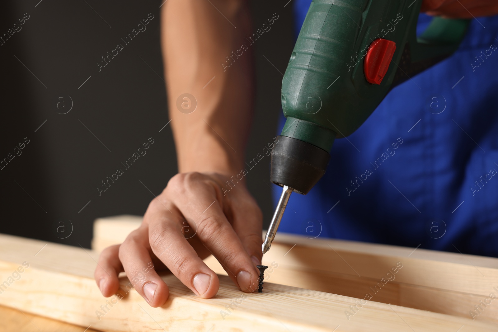 Professional repairman twisting screw into wooden plank with electric screwdriver indoors, closeup Photo of Professional repairman twisting screw into wooden plank with electric screwdriver indoors, closeup