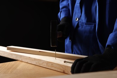 Photo of Professional repairman hammering nail into wooden plank indoors, closeup. Space for text