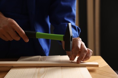 Photo of Professional repairman hammering nail into wooden plank indoors, closeup