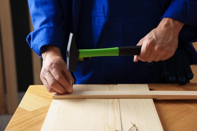 Photo of Professional repairman hammering nail into wooden plank indoors, closeup
