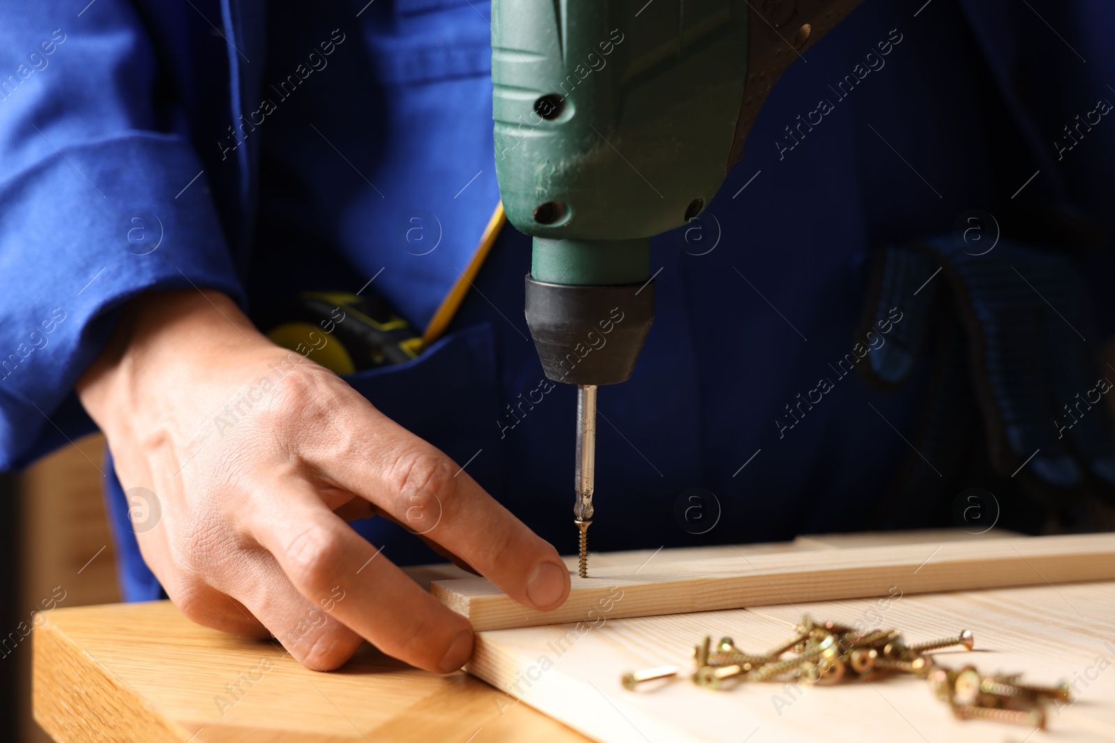Professional repairman twisting screw into wooden plank with electric screwdriver indoors, closeup Photo of Professional repairman twisting screw into wooden plank with electric screwdriver indoors, closeup